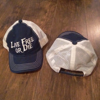 Two baseball caps on a wooden surface, one with 'Live Free or Die' text.