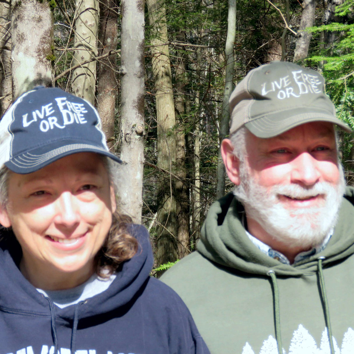 Two people wearing 'Live Free or Die' hats in a forest setting