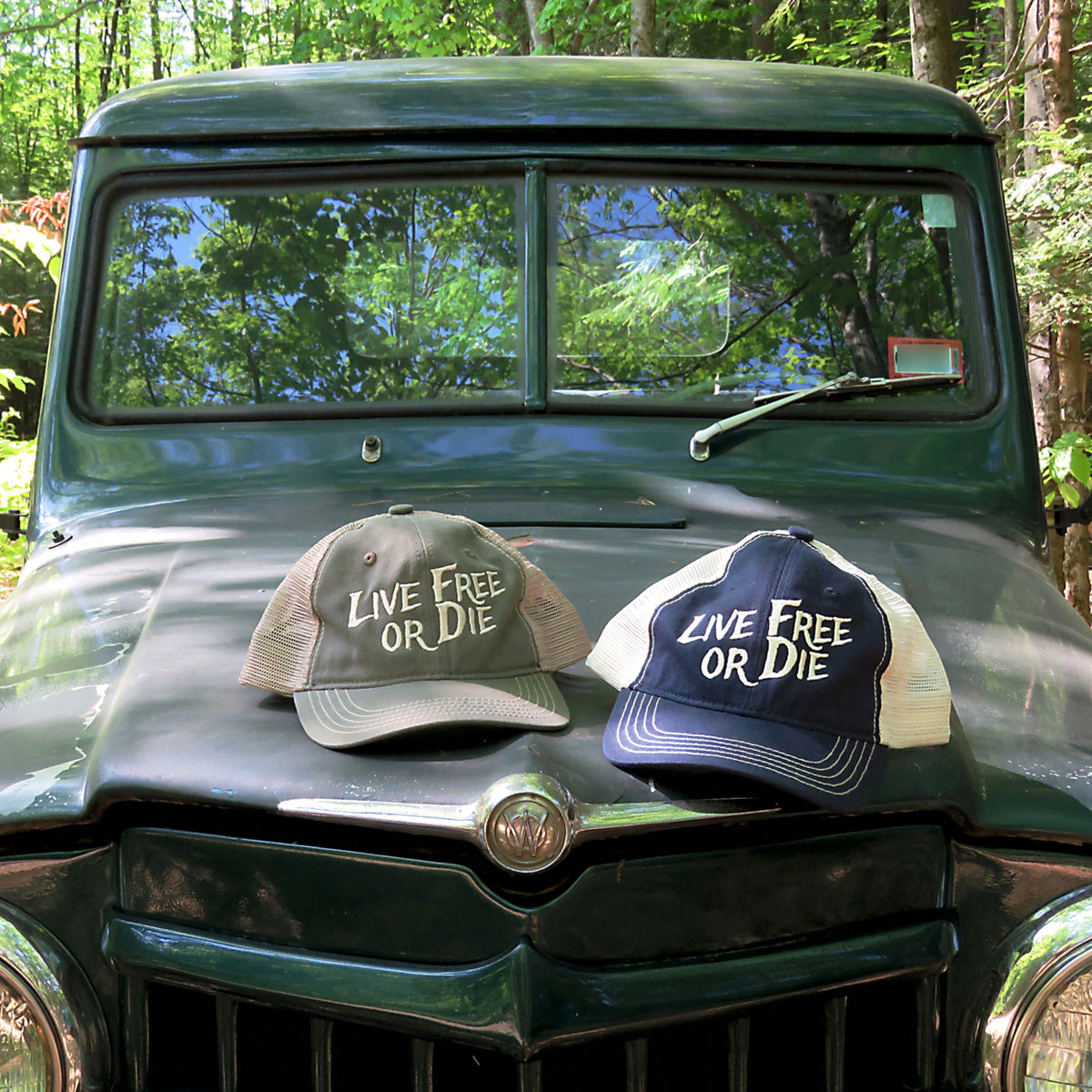 Two 'Live Free or Die' hats on the hood of a vintage green truck with a forest background.