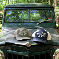 Two 'Live Free or Die' hats on the hood of a vintage green truck with a forest background.