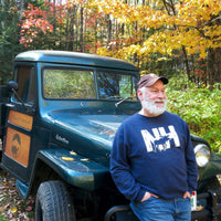 Man standing next to a vintage green truck in a forest with autumn foliage