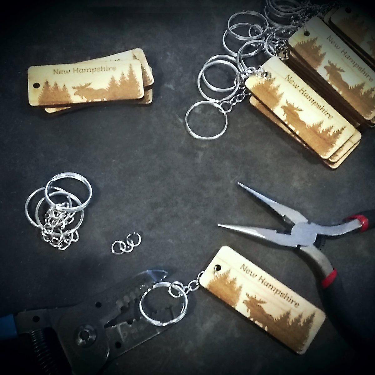 Keychains with 'New Hampshire' design on tags, pliers, and cutters on a dark surface