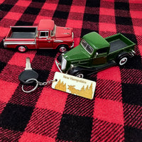 Two toy trucks, one red and one green, on a red and black checkered fabric with a keychain and 'New Hampshire' tag.