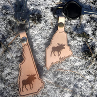 Two leather keychains shaped like the states of New Hampshire and Maine with moose designs on a textured surface.
