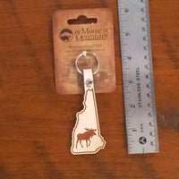 Moose-shaped keychain on a card with a ruler for scale on a wooden surface