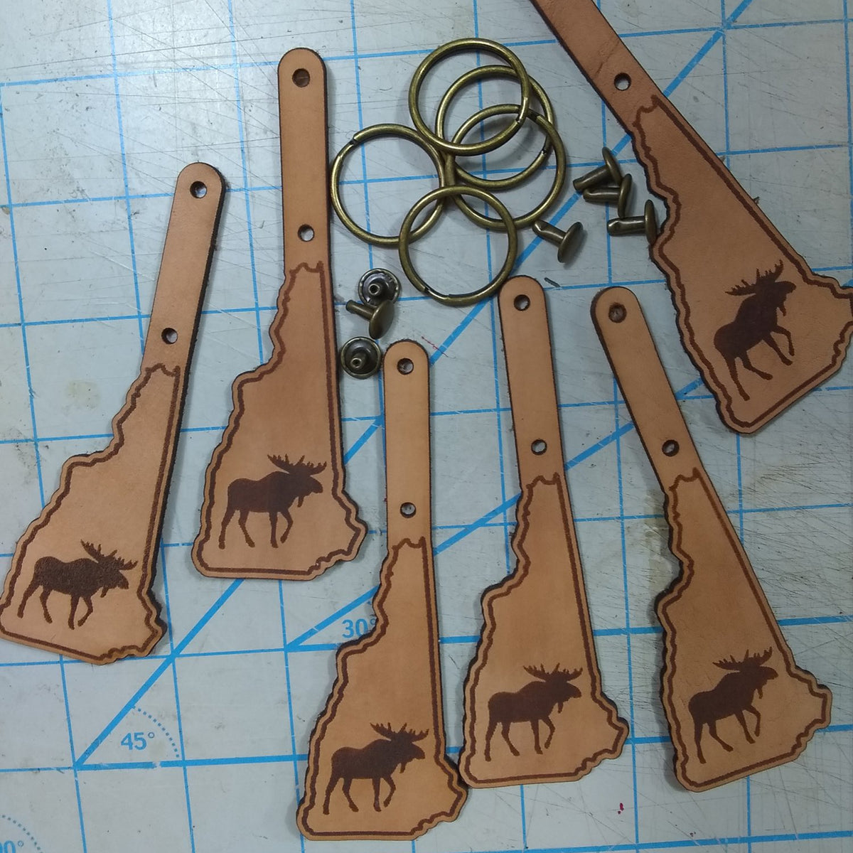 Leather keychains shaped like the state of New Hampshire with moose designs on a grid background.