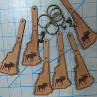 Leather keychains shaped like the state of New Hampshire with moose designs on a grid background.