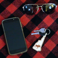 Phone, keys with a keychain, and sunglasses on a red and black checkered fabric
