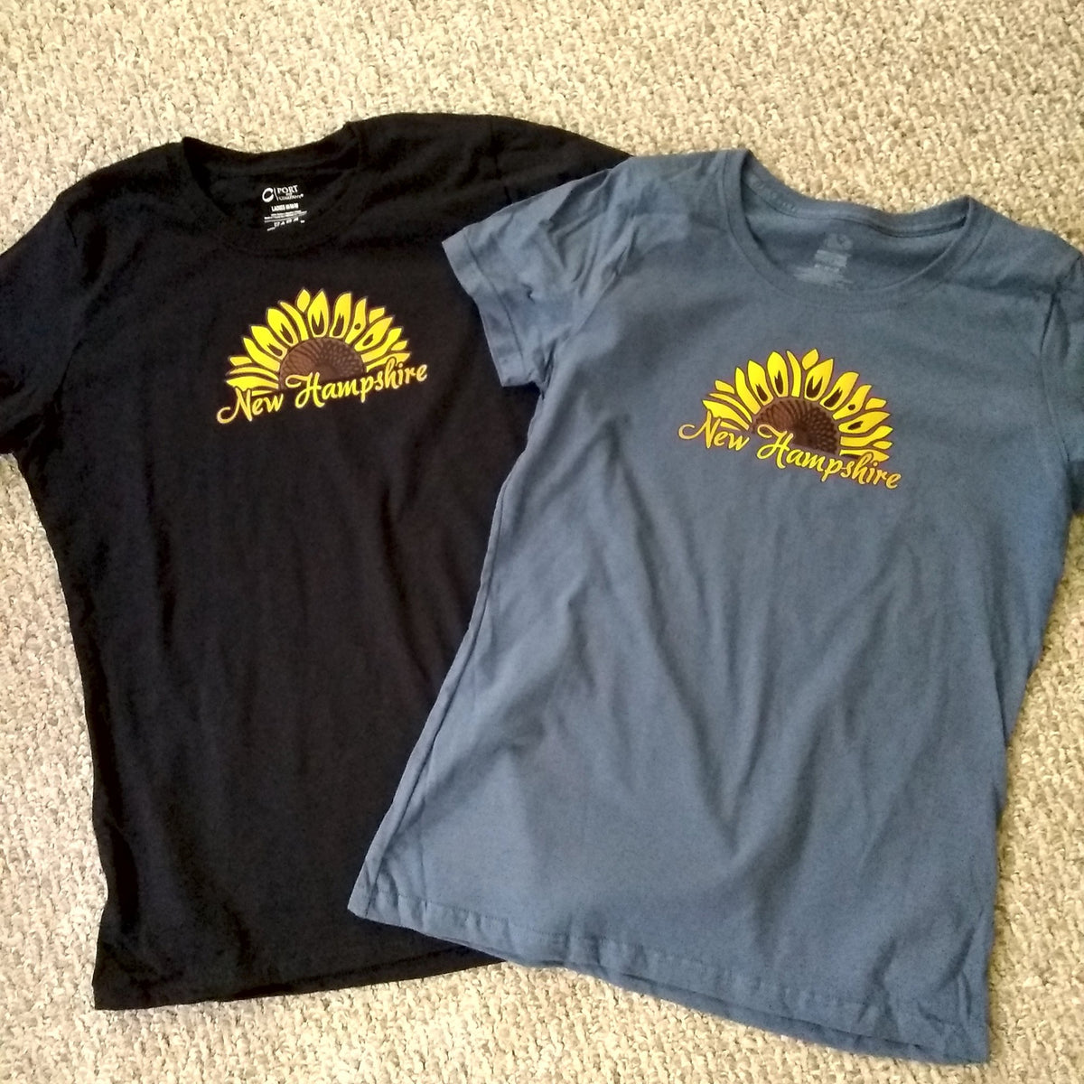 Black and blue t-shirts with sunflower design and 'New Hampshire' text on a beige carpet.