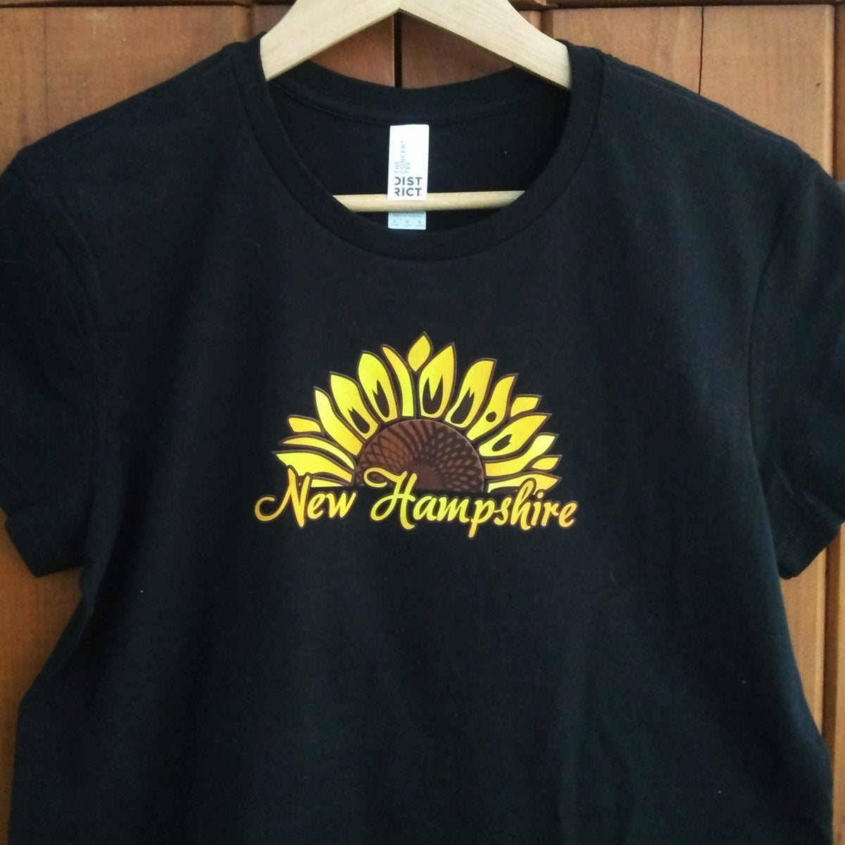 Black t-shirt with yellow sunflower design and 'New Hampshire' text on a wooden background