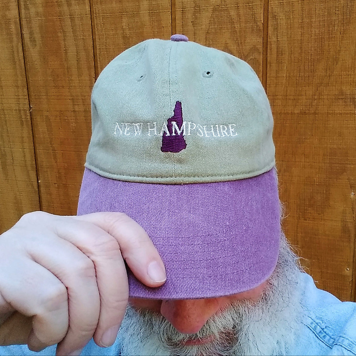 Person wearing a cap with 'New Hampshire' and a maroon outline of New Hampshire on a wooden background