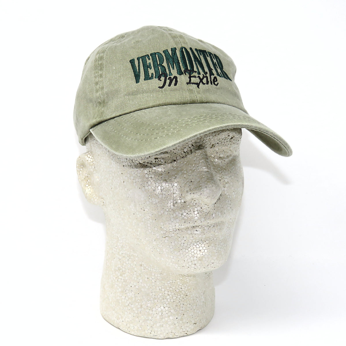 Green cap with 'VERMONT IN EXILE' text on a mannequin head against a white background