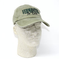 Green cap with 'VERMONT IN EXILE' text on a mannequin head against a white background