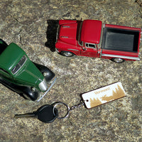Two toy trucks, one red and one green, on a textured surface with a keychain featuring 'Vermont' text.