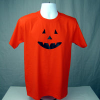 Orange t-shirt with black jack-o'-lantern face design on a mannequin against a green background