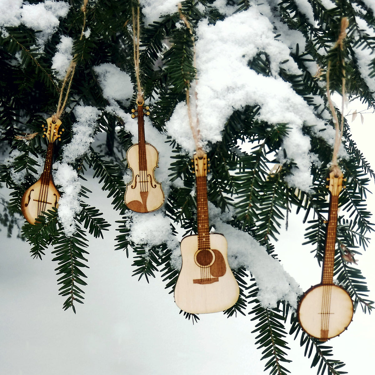 Wooden musical instrument ornaments hanging on a snow-covered tree branch.