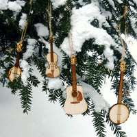 Wooden musical instrument ornaments hanging on a snow-covered tree branch.