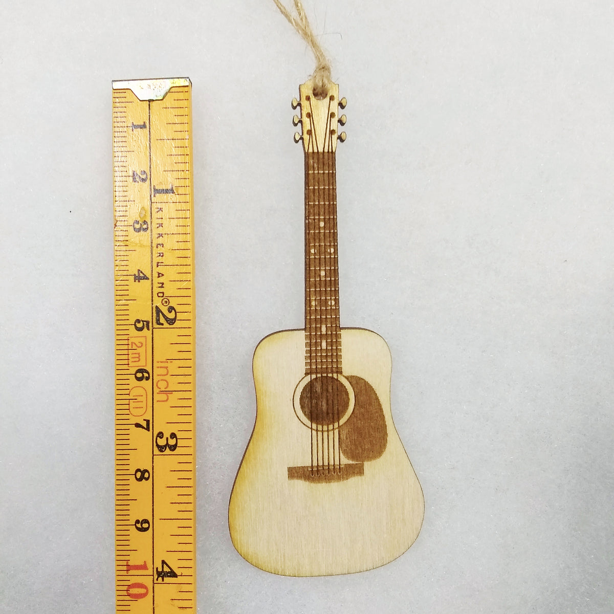 Small wooden guitar ornament next to a ruler on a light gray background