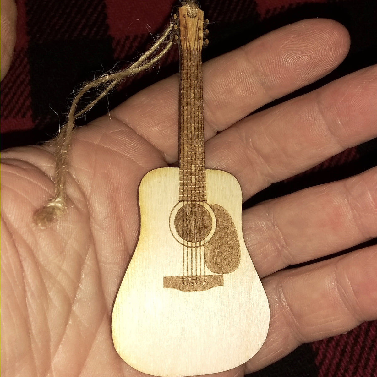 Small wooden guitar ornament held in a hand against a plaid fabric background