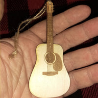 Small wooden guitar ornament held in a hand against a plaid fabric background