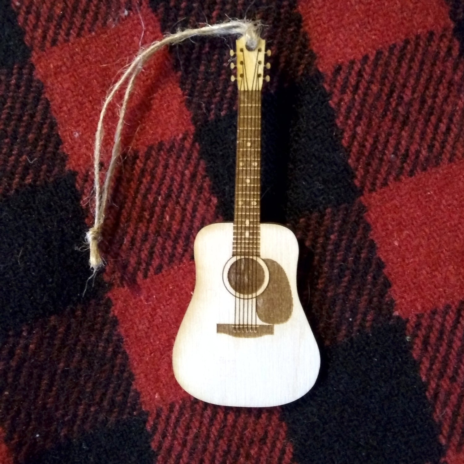Decorative guitar ornament hanging on a red and black plaid fabric background