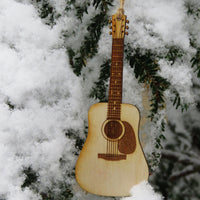 Wooden guitar ornament hanging from a tree branch with snow in the background