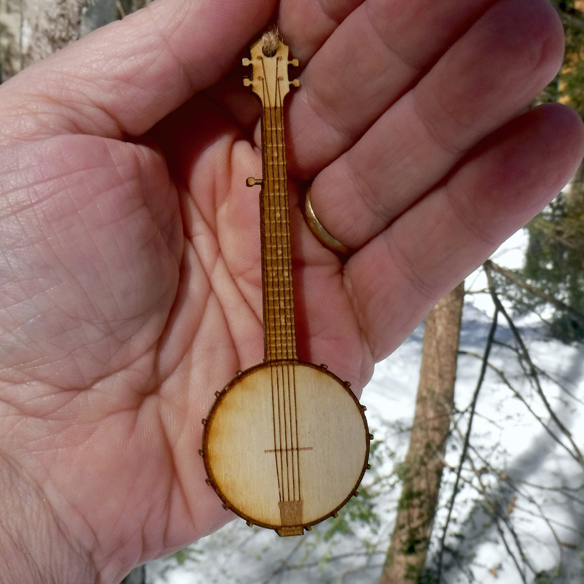 Small wooden banjo ornament held in a hand with a snowy landscape in the background
