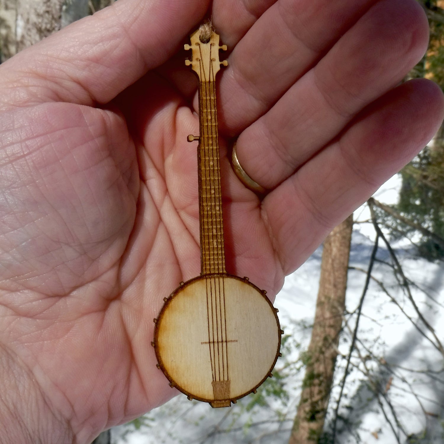 Small wooden banjo ornament held in a hand with a snowy landscape in the background