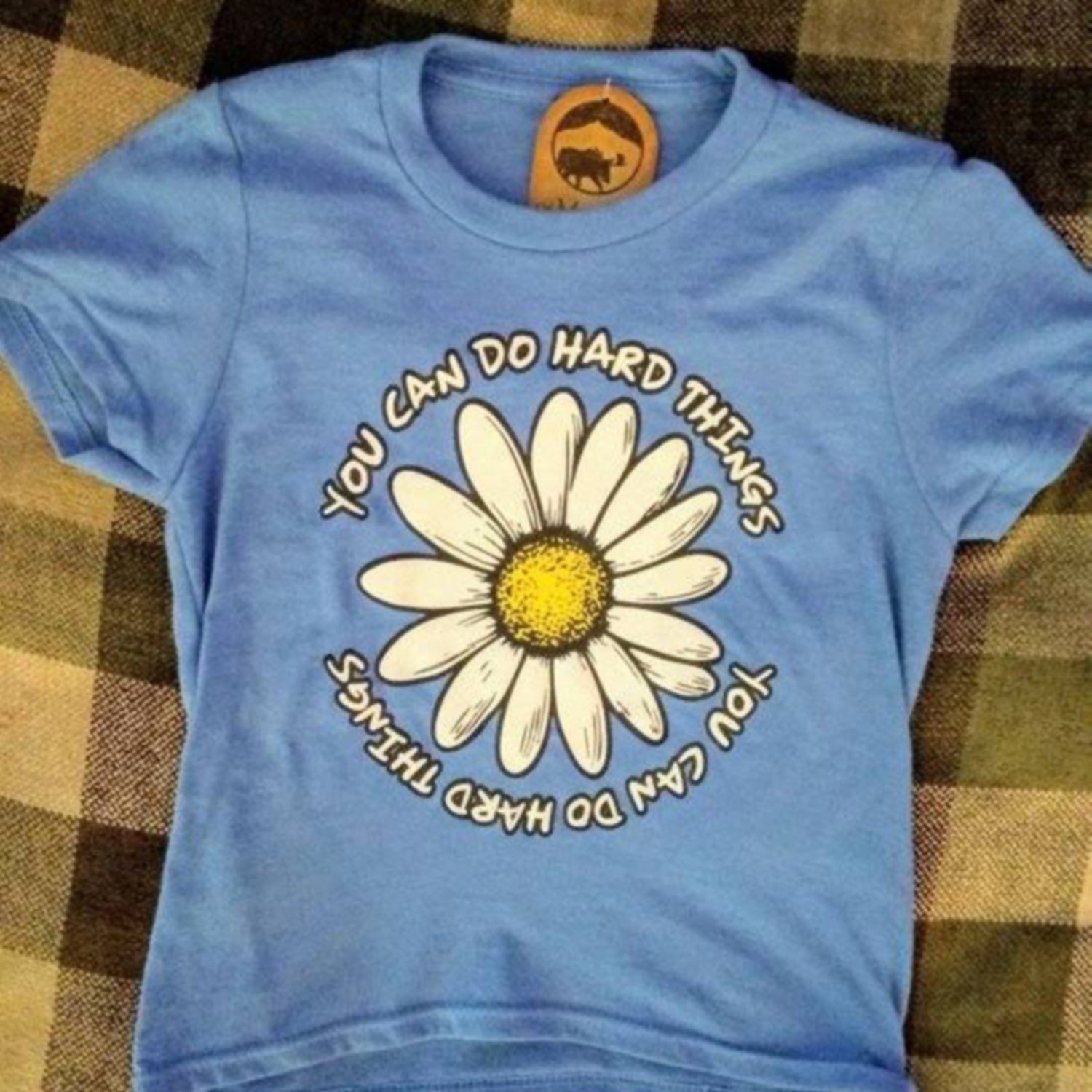 Blue t-shirt with a daisy and motivational quote on a plaid background