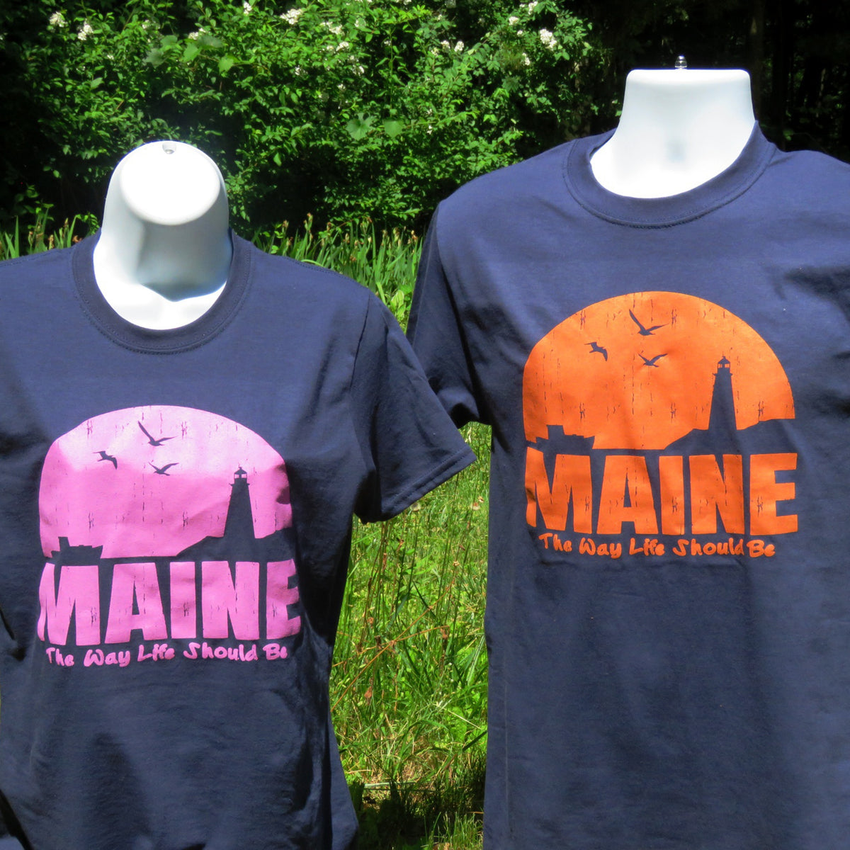 Two navy blue t-shirts with 'MAINE' graphics on mannequins outdoors.