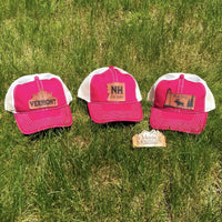 Three red and white trucker hats with state designs on a grassy background